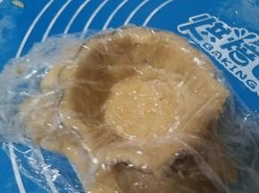 揭掉一面的保鲜膜，将另一面有保鲜膜的面朝上盖在模子里。用手按压，使饼皮跟模子紧密的贴合在一起。