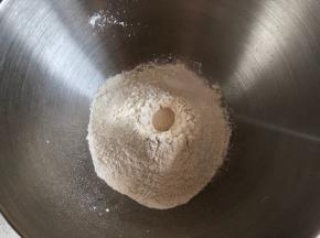 盆内倒入高粉和全麦粉，中间挖一小孔倒入活性干酵母，盐撒在一边（不要碰着酵母）