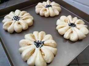 做好的花形面包生坯放入烤箱开启发酵模式进行二发，发酵至两倍大后取出，表面刷蛋液，然后在中间撒上黑芝麻装饰