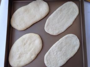 将一发后的面团移至揉面垫，平均分割成四份，搓圆后按扁，用擀面杖擀成长条状，依次摆入不沾烤盘，放入烤箱开启发酵档进行二发