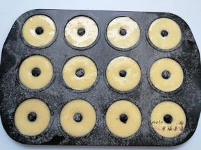 甜甜圈模具提前刷一层黄油，并筛一层低筋面粉防粘，然后依次挤入面糊，挤一半的时候撒上一些蔓越莓干，然后再继续挤满