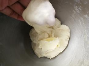 约8分钟后，面团能拉出粗膜，加入盐和软化的黄油，继续和面