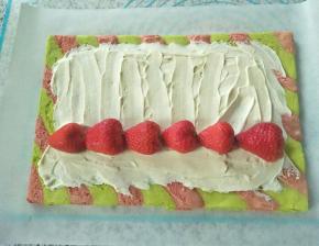 把蛋糕四条边切掉，均匀铺上一层奶油，摆上一排草莓，借助擀面杖把蛋糕卷起来