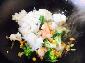 放入炒好的虾仁翻炒均匀。 改中火，放入米饭，将米饭和蔬菜炒匀，放入适量的盐调味。