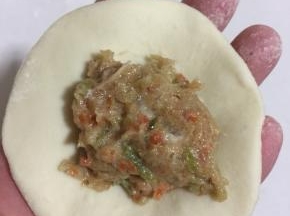 取一个面团，揉圆，擀成中间厚，两边薄的面片。放一勺肉馅儿在面片中间。