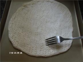 擀面杖涂抹一点黄油、防粘，取出面团，在案板上滚圆排气，盖上保鲜膜静置松弛15分钟，再用擀面杖擀薄至2厘米左右厚的圆饼、用叉子在面饼的表面戳些小孔，帮助排气