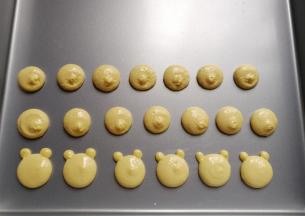 先用大份蛋糊在不粘烤盘上挤上圆形，再用小份蛋糊在圆形上方两侧挤上两个小圆点，这样小熊胚形就出来了；