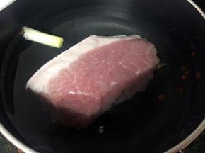 猪后腿肉洗净放入锅中，加适量清水，一节葱头、几粒花椒，一小块姜煮开，转小火将肉煮过心捞出。
