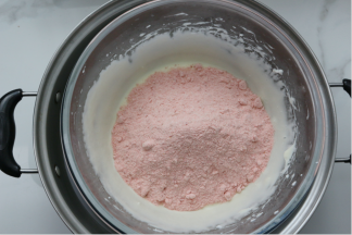 再倒入奶粉和冻草莓粉，用硬刮刀搅拌均匀，或者带上一次性手套将其混合均匀