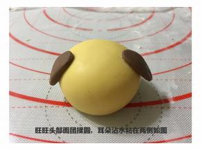 发酵好的黄色大面团分成50克一个的小面团制作金狗的头部。可可粉制作好的耳朵（不到1克/个）用手指沾水粘在头部的两侧。沾水的目的主要是粘合的比较牢固