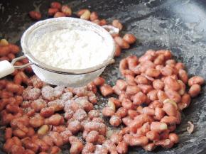 待糖汁包裹住花生米，边翻炒边筛入干淀粉