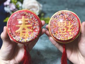 糖霜完全干了以后，在透明盖子里倒入适量彩珠糖，然后再糖霜饼干的周围再挤入一圈红色糖霜，为了粘住盖子，把装了彩珠糖的盖子扣上去，按压一下，等待糖霜干爽即可