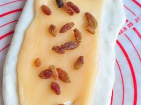 将麻糬馅也分成三份，擀开后放在面皮上，最上面撒些葡萄干。