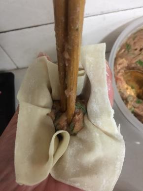 用筷子将馅料往下按压，五指将馄饨皮往中间捏。