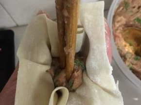 用筷子将馅料往下按压，五指将馄饨皮往中间捏。