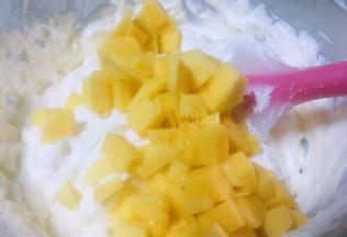 奶酪糊和奶油充分拌均后倒入3分之二的芒果丁再次搅拌均匀