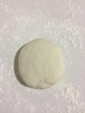 案板上撒少许面粉，把醒好的面团取出来，多揉一会儿，再按压一下。