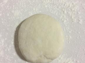 案板上撒少许面粉，把醒好的面团取出来，多揉一会儿，再按压一下。