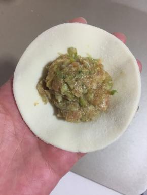 取一个饺子皮，放一勺肉馅儿，按压一下。