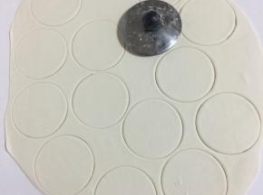 在面片上撒少许面粉，再用茶壶盖按压出圆圆的饺子皮。嘻嘻，非常的省事方便吧？（面皮撒少许面粉再按压，以免压好的饺子皮粘在一起。按压后多余的面片揉圆，擀成面片，再继续按压成饺子皮，直到所有的面团都按压完为止。）