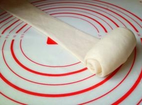 取一块面团用擀面杖擀长舌状，再卷起来，从上往下卷，依次做完。