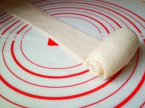 取一小块面团擀成长舌状，再卷起来。从上往下卷，或者从下往上卷都可以，没有特别要求。 这样反复两次，也就是图中卷好的面团卷再次用擀面杖擀长舌状，再卷起来。把3块面团依次做完。