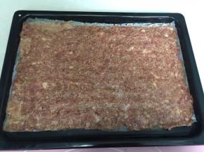 然后撕去一层油纸，将擀好的猪肉放入烤盘里