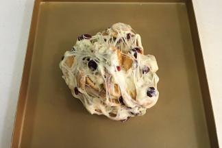 把雪花酥团倒入不粘烤盘内，用双手不停往外翻，直到饼干和坚果料都被千丝万缕的糖包裹住。