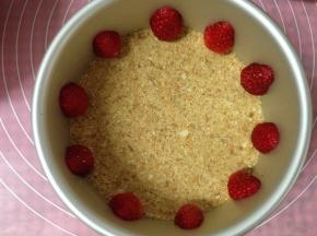 将草莓去蒂从中间切开成两半，将冰箱中冷藏好的饼干底取出，摆放好草莓的位置