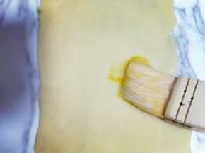 之后将本色面团用擀面杖擀成长舌状，刷上一层薄薄的蛋液。