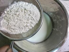 不锈钢盆里倒入牛奶，筛入低筋面粉，为了做出蓬松的口感，面粉要用低筋的，用橡皮刀把低筋面粉和牛奶混合均匀备用。