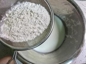 不锈钢盆里倒入牛奶，筛入低筋面粉，为了做出蓬松的口感，面粉要用低筋的，用橡皮刀把低筋面粉和牛奶混合均匀备用。