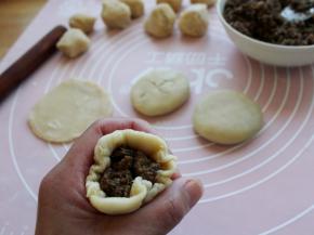 取一个小面剂擀圆（案上和擀面杖上用一点点薄粉），放入馅料约20克包起来。
捏合处做为底面，轻轻地按扁，整理成圆饼。