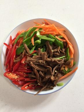 浸泡好的萝卜干挤干水分切成条，红尖椒和青椒切成丝，胡萝卜也切成丝备用。