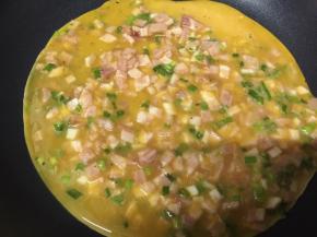 小火，热锅冷油，倒入香菜培根鸡蛋液
迅速均匀摊平