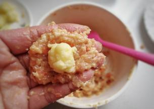 取适量肉馅放在手上摊平，摆上奶酪小团子，然后包起来团成丸子