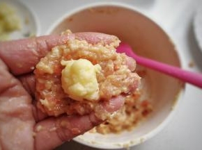 取适量肉馅放在手上摊平，摆上奶酪小团子，然后包起来团成丸子