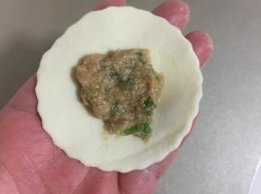 取一个饺子皮，在中间抹上适量的馅儿，按压一下。