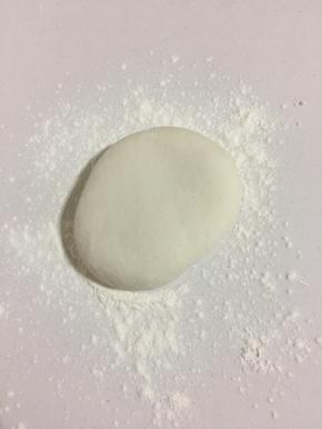 案板上撒少许面粉，把醒好的面团取出来揉匀，按扁。