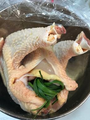 把腌制入味的鸡取出，用厨房纸擦干表面，把葱打成结，和姜片一起塞入鸡肚子里。