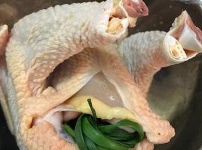 把腌制入味的鸡取出，用厨房纸擦干表面，把葱打成结，和姜片一起塞入鸡肚子里。