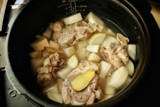 煮过的骨头放入压力锅，白萝卜也一并放入，加入葱段和姜片，加入足量的水。