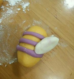 搓圆后用拇指压一下，稍微扁一些。然后沾到蜜蜂身上，两根紫色线的中间位置。