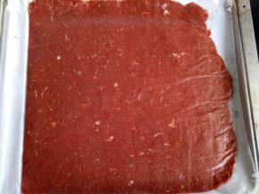 把擀好的肉脯整片放到烤盘里，将上面的一层油纸揭开，将多余的油纸剪掉或者压到烤盘下，肉脯裸露在外面