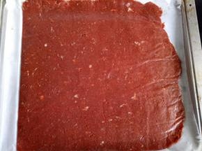 把擀好的肉脯整片放到烤盘里，将上面的一层油纸揭开，将多余的油纸剪掉或者压到烤盘下，肉脯裸露在外面