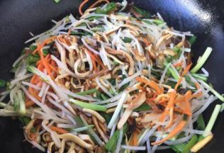 放入胡萝卜丝煸炒至断生，放入绿豆芽、香干丝、韭菜、鸡蛋饼丝，迅速翻拌。