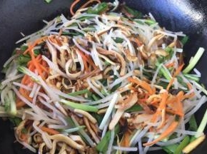 放入胡萝卜丝煸炒至断生，放入绿豆芽、香干丝、韭菜、鸡蛋饼丝，迅速翻拌。