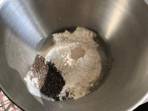 厨师机面盆内倒入清水，然后倒入高筋面粉和全麦粉，倒入炒香放凉的奇亚籽，盐和糖对角线放置，面粉中间挖一小孔倒入活性干酵母