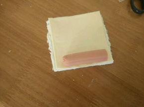 在吐司上放一片芝士和半根火腿肠。然后卷起来。