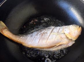 开大火，置锅，锅热，放入适量的油，当油温六成热时放入黄花鱼。 往热油锅里放鱼时请注意，要用双手拎着鱼的头和鱼尾，轻轻放入油锅里。 刚刚放入鱼后千万不要急于翻动，因为铲子是凉的，鱼肉会马上锁住铲子，也就是粘铲子。 煎约1分钟后，请观察鱼身边的颜色，如果发黄色，说明可以翻动。